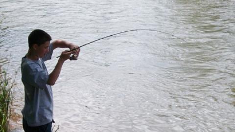 youth reels in his line pulling a fish just up out of the water.