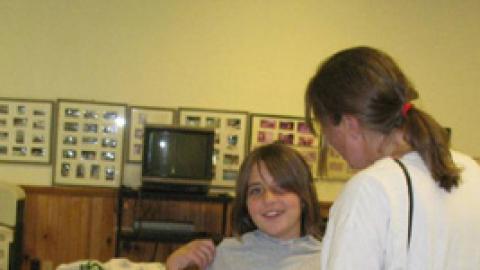 camper holds a 4-H Camp t-shirt up to her chest to see if it's the right size as a parent looks on.
