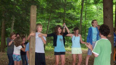 Youth holding hands on wire cable between trees a few inches off the ground.