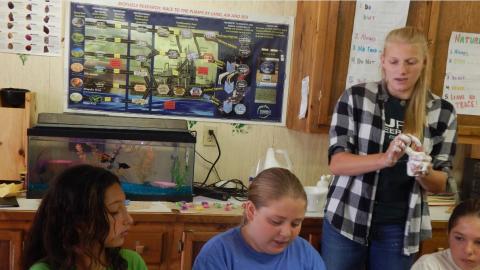 Counselor holds and discuses a science experiment as campers around a table hold their own experiments.