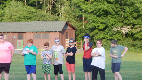 Cabin group stand in a line wearing sunglasses and smiling while one reads from a paper.