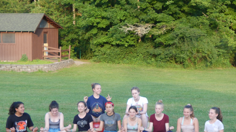 Cabin group sitting cross-legged with eyes closed holding fingertips together.