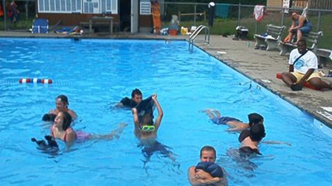 youth swimming in the pool under the supervision of a lifeguard on the pool deck. Water is sparkling blue.