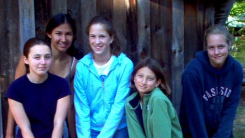 four youth standing with a counselor leaning on tennis rackets