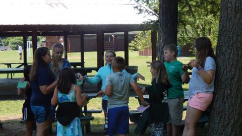 Group of youth with counselor near a tree with arms raised at their sides.