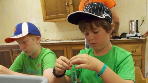 camper dipping wick into liquid wax to make candles.