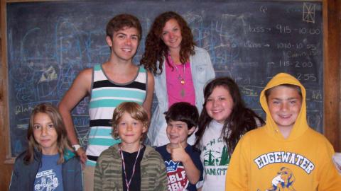 campers pose in front of a chalk board with smiling faces 