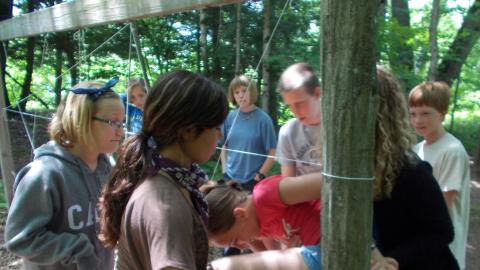 campers climbing through rope obstacle course with campers watching in background