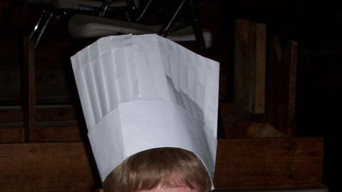 young man in a paper chefs hat displaying his parfait and smiling. 