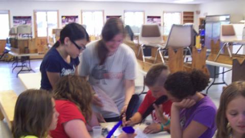 campers sitting around a table using quill feather pens.