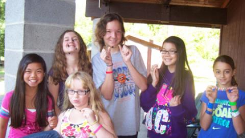 Six youth pose together showing off craft necklaces and smiling.
