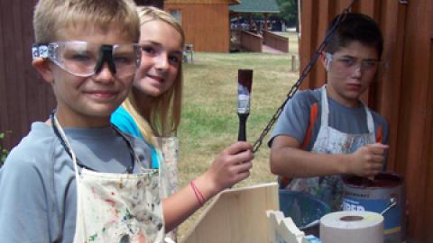 Three youth at painting station behind science center.