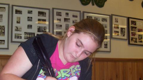 Close-up of youth writing with quill pen. 