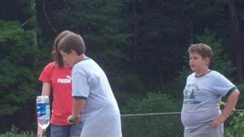Youth pumping air into a bottle filled with water as two campers watch.