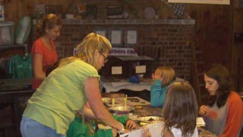craft director standing over camper with others seated around the table working with foil pie tins.