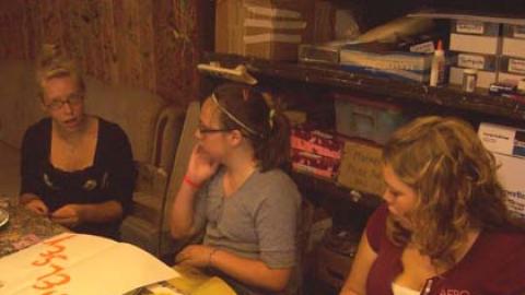 Three youth sit around a table making name signs in craft hall.