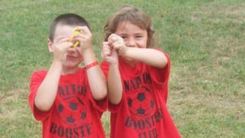 Two youth standing in hula hoop hiding their faces with something in their hands.