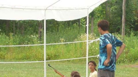youth laying in prone position aiming their air rifles under the supervision of a counselor.
