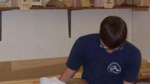 Staff holding plywood while youth uses jigsaw.