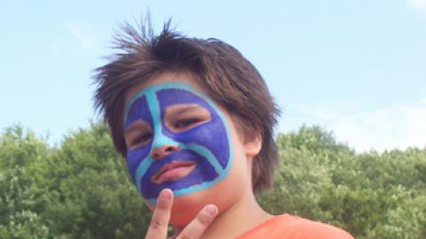 Youth with fully painted face giving a peace sign to the camera.