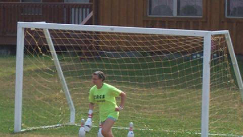 camper runs from the soccer goal carrying a bowling pin and leaving three bowling pins behind.