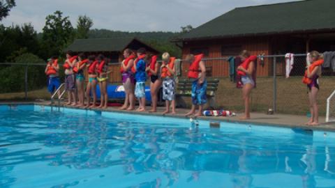 campers standing poolside with life jackets on.