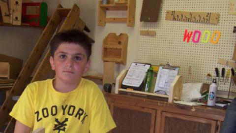 Camper standing with wooden bookshelf that has letters JMS cut out from the board.