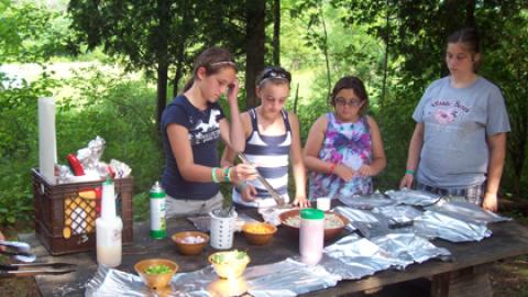 Yoyth at a table adding fillings to tin foil packet.