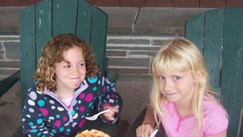 two youth sitting in Adirondack chairs eating pizza they made in chef's club.