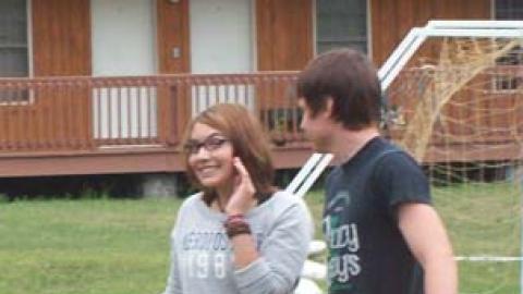 Smiling camper stands with another camper holding a ball. 