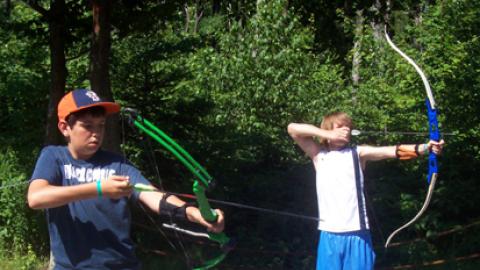 Youth standing on line drawing back their bow.