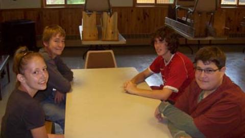 group of counselor in training youth sit together at a table and smile at the camera.