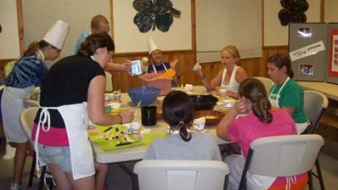 Youth around a table working with a mix of ingredients wearing aprons. 