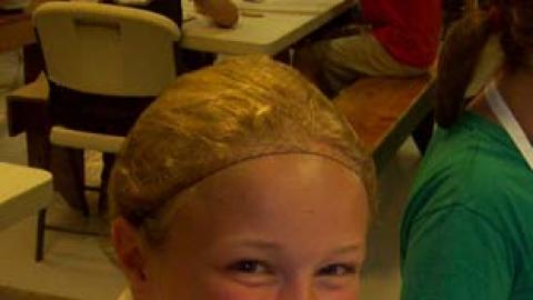 Youth smiling and giving thumbs up to the camera holding a parfait of fresh fruit.
