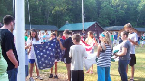 Campers work together to raise the 4-H and American flags while the rest of camp looks on.
