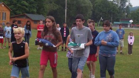 colorguard approaches the flagpole with folded american and 4-H flags. Leader is smiling wide.