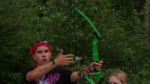 counselor demonstrates how to nock an arrow on their bow as campers watch.