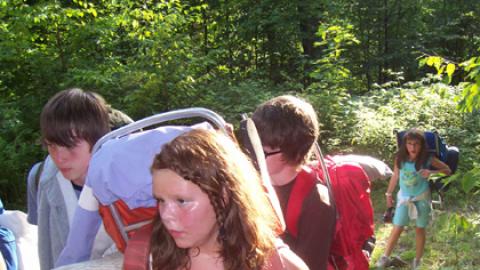 Youth hiking up a trail wearing backpacks.