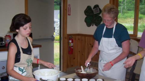 Two youth at table scooping batter into muffin tins.