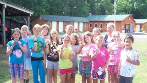 Group of youth smiling outside with craft director and showing off craft project necklaces.