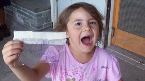 Smiling camper holding up plastic bag that says "front teeth" with two teeth in it.