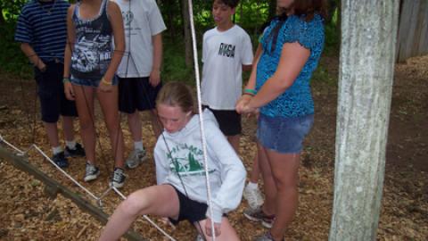 camper stepping through a hole in the spiders web while their team looks on.