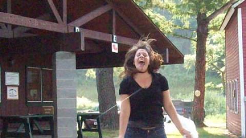 Counselor jumping into air sticking out tongue holding a garbage bag in each hand.