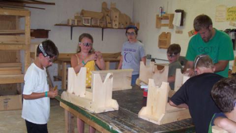 Two staff oversee youth making finishing touches on their woodworking benches.