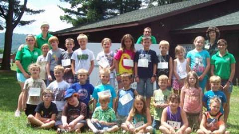 Day campers posing beside dining hall with camp staff.