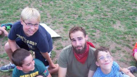 three youth sit near a counselor all looking up from the ground and smiling.
