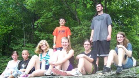 Youth standing on large rock at top of forest hike.