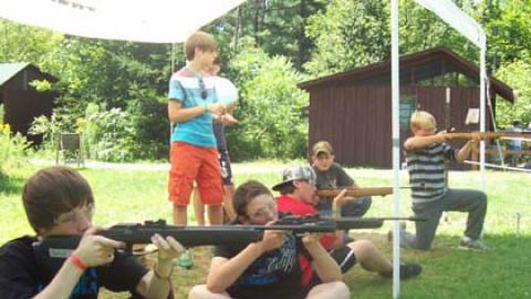 Youth sitting crossed legged taking aim with air rifles.