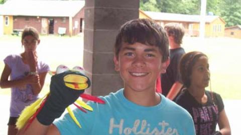 smiling youth shows off a sock puppet with colorful feathers.