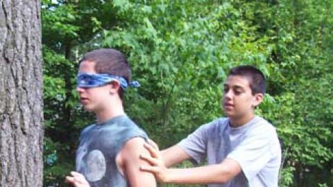 One youth leads another blindfolded youth to a nearby tree during a team challenge activity.